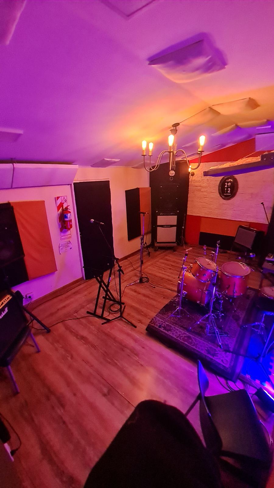 Sala de ensayo con batería y equipamiento, iluminación violeta